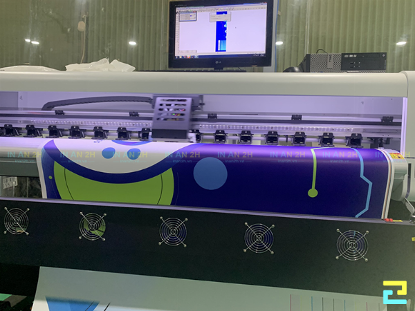 Một chuyên gia in ấn đang tư vấn cho khách hàng, tay cầm mẫu vật liệu bạt Hiflex và giấy PP để so sánh trực tiếp