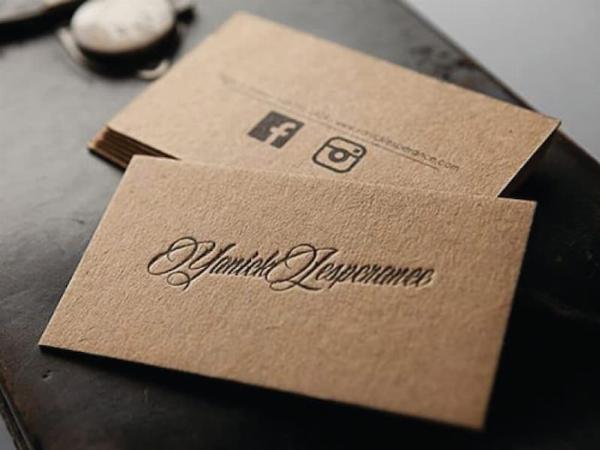 Một chồng name card in trên giấy Kraft màu nâu đặc trưng, với thiết kế đơn giản, tinh tế, đặt trên nền gỗ mộc